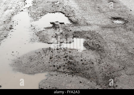 Grandi buche in rotto una strada asfaltata riempito con acqua piovana fangosi. Copia area spazio per la costruzione stradale progetti di riparazione e biella Foto Stock