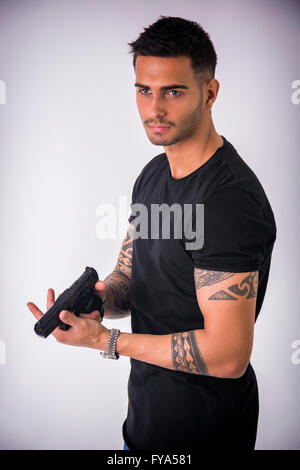Giovane uomo bello puntando la pistola, indossando t-shirt nera su sfondo chiaro Foto Stock