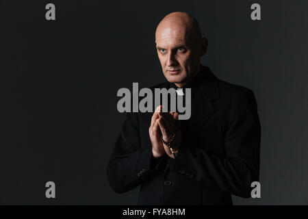 Sacerdote e pregando su sfondo nero Foto Stock