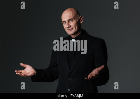 Sorridente sacerdote e invitante è su sfondo nero Foto Stock