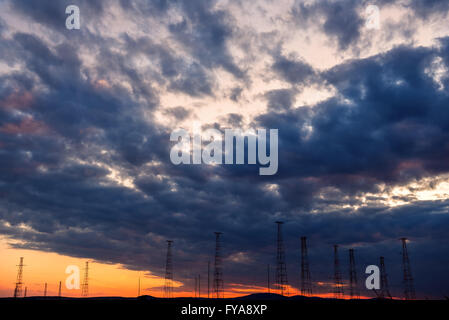 Alta tensione delle linee di trasmissione su arancio e blu cielo Foto Stock