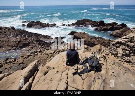 Una donna seduta da sola sul bordo di una scogliera rocciosa a Salt Point State Park nel nord della California, Stati Uniti d'America. Foto Stock
