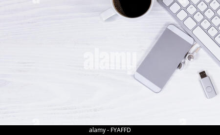 Vista aerea del desktop bianco con parziale della tastiera del computer, telefono cellulare, caffè, unità thumb e auricolari. Foto Stock