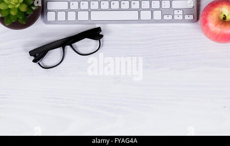 Vista aerea del desktop bianco con parziale della tastiera del computer, Apple, gli occhiali da lettura e neonato impianto nella parte superiore del telaio. Foto Stock