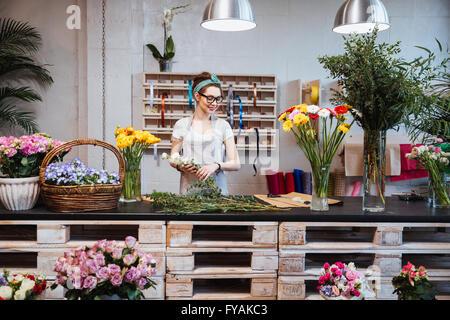 Allegro bella giovane donna fioraio in bicchieri sorridente e lavorando in negozio di fiori Foto Stock