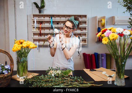 Felice carino donna giovane fioraio godendo la rosa bianca nel negozio di fiori Foto Stock