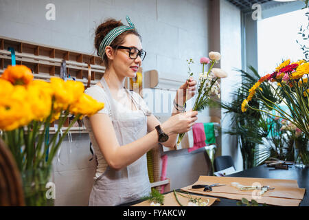 Felice affascinante giovane donna fioraio azienda bellissimi fiori e rendendo bouquet in negozio Foto Stock
