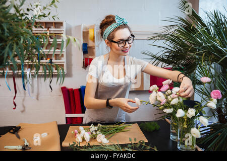 Sorridente attraente giovane donna fioraio e lavoro rendendo bouquet nel negozio di fiori Foto Stock