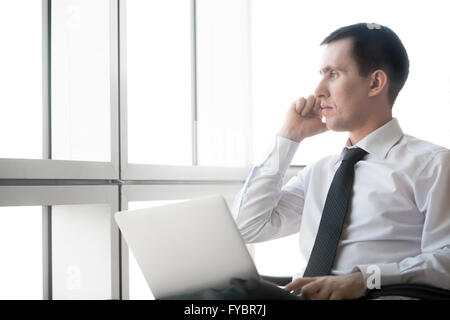 Ritratto di grave bel giovane uomo d affari lavorando sul computer portatile ed effettuare una chiamata. Imprenditore caucasico Foto Stock