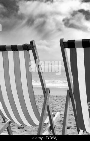 Una coppia di strisce di sedie a sdraio al vento sulla spiaggia di Bournemouth, Regno Unito Foto Stock