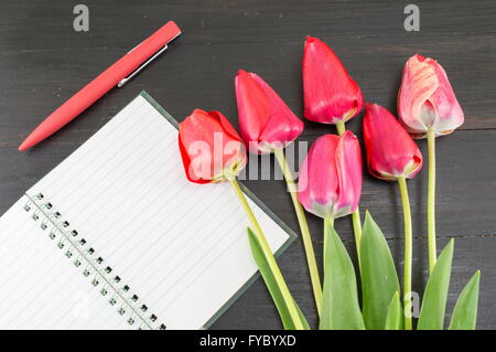 Tulipani rossi e un notebbok al buio su un tavolo di legno Foto Stock