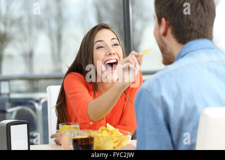 Giocoso giovane mangiare patate di chip e scherzando cercando reciprocamente in una data in un coffee shop Foto Stock