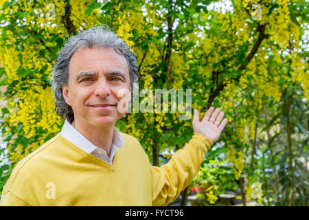 Uomo di mezza età che mostra il Maggiociondolo in giardino verde Foto Stock