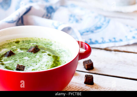 Zuppa di spinaci con crostini in rosso ciotola sul tavolo di legno Foto Stock