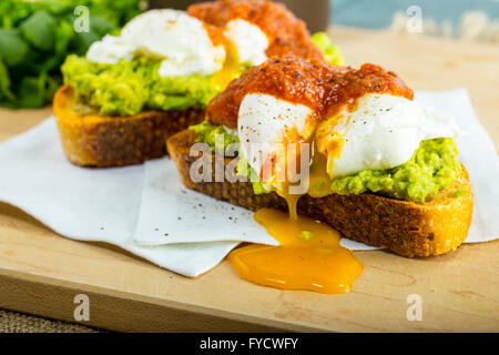 Avocado Toast con uova in camicia sul bordo di taglio Foto Stock