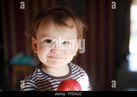 Quindici mesi giovane capretto apple tiene in mano prima di godere di essa, guarda nella telecamera con sguardo gentile e curiosità affascinante sorriso Foto Stock