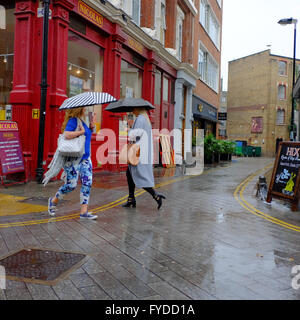 Due donne con ombrelloni passando l un l altro come di attraversare una strada a Londra Foto Stock