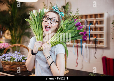 Funny felice giovane donna fioraio tenendo due mazzi di tulipani nel negozio di fiori Foto Stock