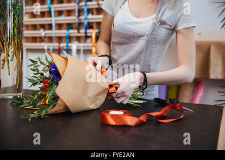 Le mani della giovane donna fioraio permanente e la realizzazione bouquet di fiori in negozio Foto Stock