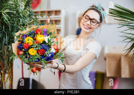 Allegro piuttosto giovane donna fioraio in bicchieri che mostra bouquet di fiori colorati Foto Stock