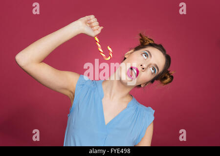 Divertente giocoso giovane donna divertendosi con candy cane su sfondo rosa Foto Stock