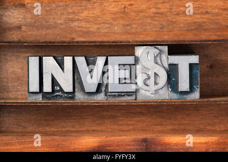 Investire parola fatta da metallico tipo di stampa in rilievo sul vassoio in legno Foto Stock