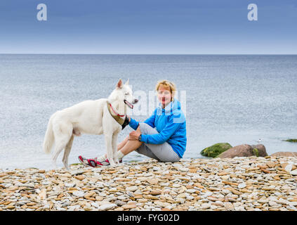Una donna si siede con un cane sulla spiaggia Foto Stock