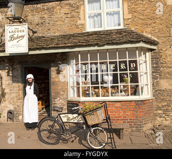 Negoziante giovane donna in vecchio stile di abbigliamento tradizionale al di fuori del villaggio panificio, Lacock, Wiltshire, Inghilterra, Regno Unito Foto Stock