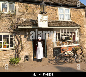 Negoziante giovane donna in vecchio stile di abbigliamento tradizionale al di fuori del villaggio panificio, Lacock, Wiltshire, Inghilterra, Regno Unito Foto Stock