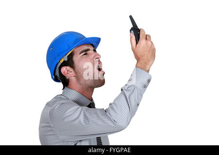 Imprenditore arrabbiato che indossa un casco e grida al suo walkie-talkie Foto Stock
