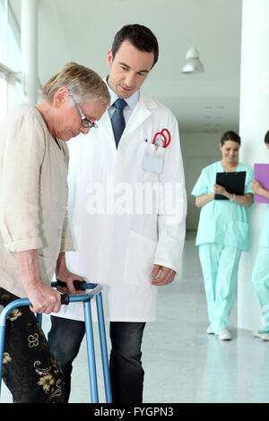 Donna anziana utilizzando un telaio a piedi in un ospedale Foto Stock