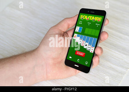 Stretta di mano azienda mobile smart phone con carte gioco app sullo schermo. Tutti i grafici dello schermo sono costituiti. 3D generati. Foto Stock