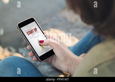 Donna che mantiene uno smartphone con start up sullo schermo. Tutti i grafici dello schermo sono costituiti. Foto Stock