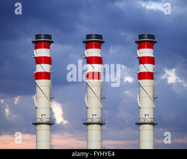 Camini industriali sul cielo nuvoloso al tramonto Foto Stock