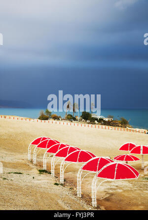 Red ombrelloni da spiaggia sulla costa del Mar Morto a thunder-storm Foto Stock
