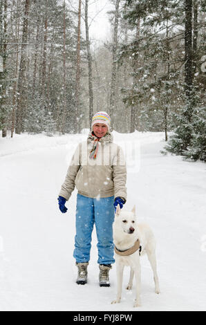 Donna con un cane in una passeggiata nel bosco durante una nevicata Foto Stock