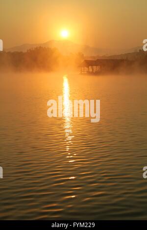 Misty tramonto tropicale sul lago con casa in legno in Mae Ngad diga e serbatoio, Chiang Mai, Thailandia Foto Stock