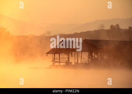 Misty tramonto tropicale sul lago con casa in legno in Mae Ngad diga e serbatoio, Chiang Mai, Thailandia Foto Stock
