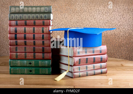 Graduazione mortarboard sulla parte superiore della pila di libri su sfondo astratto della parete Foto Stock