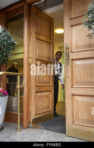 Un hotel di facchinaggio o Porter aprendo lo sportello anteriore di un hotel per ospiti nel Regno Unito. Foto Stock