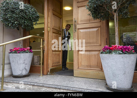 Un hotel di facchinaggio o Porter aprendo lo sportello anteriore di un hotel per ospiti nel Regno Unito. Foto Stock