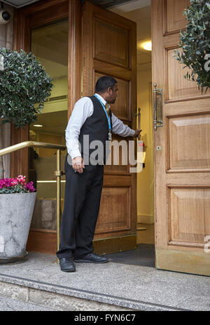 Un hotel di facchinaggio o Porter aprendo lo sportello anteriore di un hotel per ospiti nel Regno Unito. Foto Stock