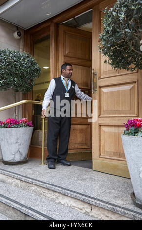 Un hotel di facchinaggio o Porter aprendo lo sportello anteriore di un hotel per ospiti nel Regno Unito. Foto Stock