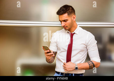 Bel giovane imprenditore nel suo ufficio e di digitazione tramite telefono cellulare, guardando verso il basso, gravi Foto Stock