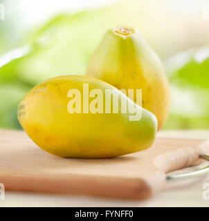 Due intere fresche dolci papaia tropicale su un tagliere di legno fotografato all'aperto contro il verde Foto Stock