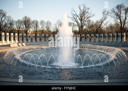 WASHINGTON, DC, Stati Uniti: La fontana principale del National World War II Memorial sul National Mall di Washington DC. I getti d'acqua spruzzano verso l'alto dal bacino circolare, circondato da 56 pilastri di granito che rappresentano gli stati e i territori degli stati Uniti. Il monumento a Washington è visibile sullo sfondo. Foto Stock