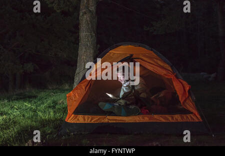 L'uomo guarda il suo smartphone in una tenda di notte. Foto Stock