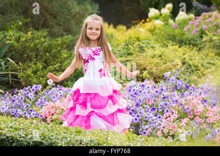 Piccolo felice ragazza in un abito rosa a letto di fiori Foto Stock