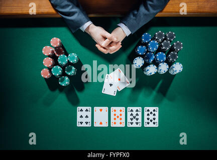 Giocatore di poker con le mani le schede e le pile di chips tutto sul tavolo verde, vista dall'alto Foto Stock