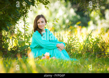 Una ragazza in un abito lungo seduto sull'erba nel bosco in tempo soleggiato Foto Stock